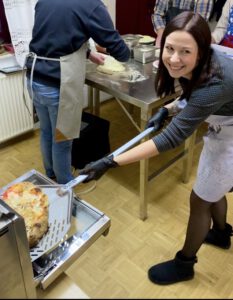 Glückliche Kursteilnehmerin beim Pizza Workshop zieht eine frisch gebackene Pizza aus dem Ofen